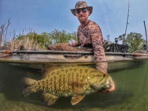 Matt Nelson sitting in kayak while holding smallmouth bass just under the water.