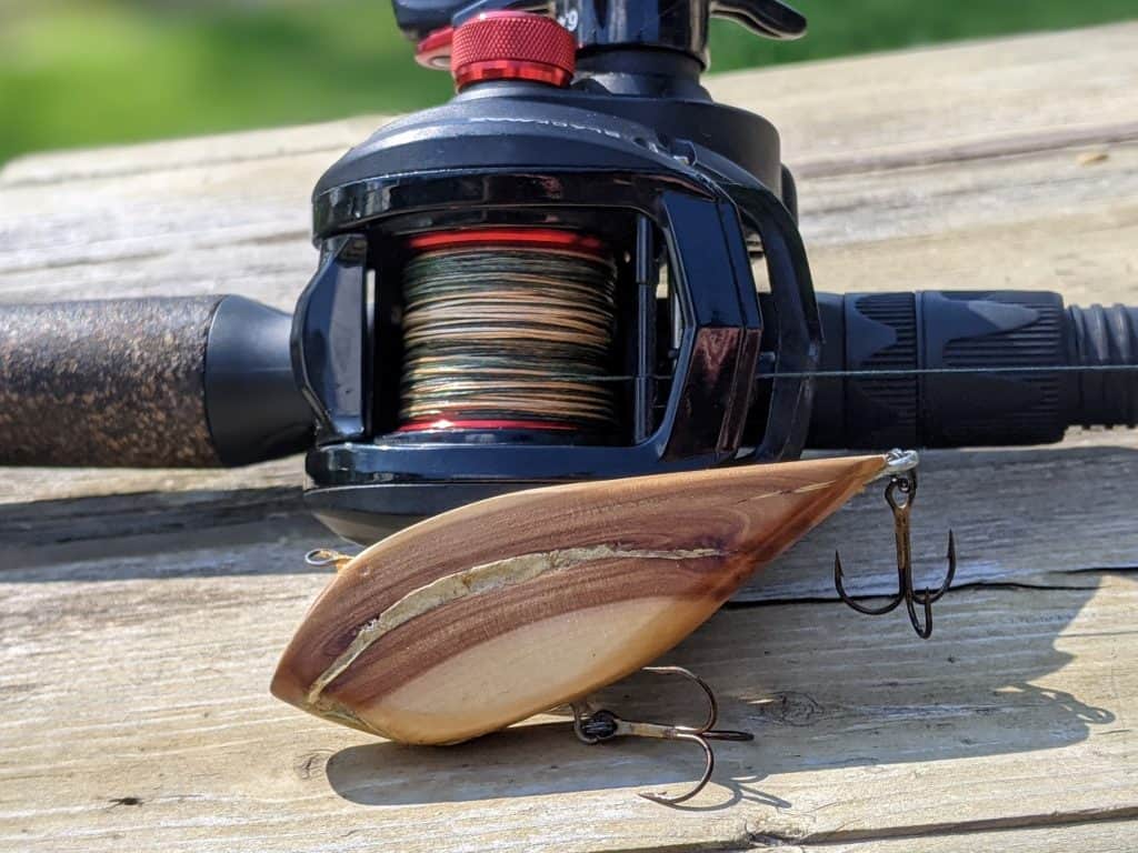 handmade wooden lipless crankbaits for bass sitting in front of a Abu Garcia Black Max baitcaster reel
