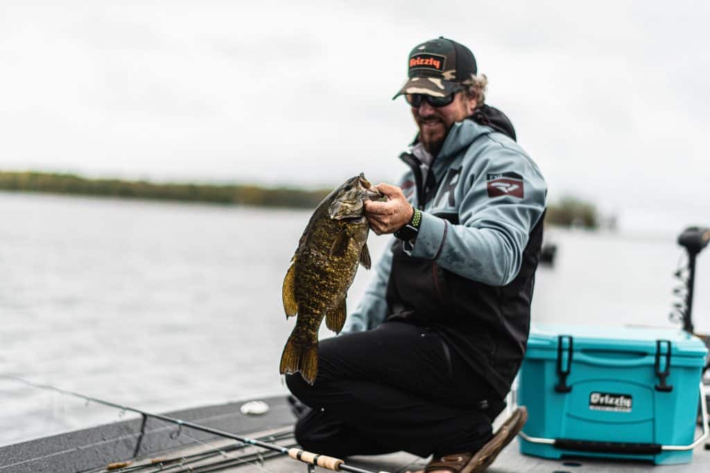 matt peters holding a smallmouth bass next to a teal grizzly cooler
