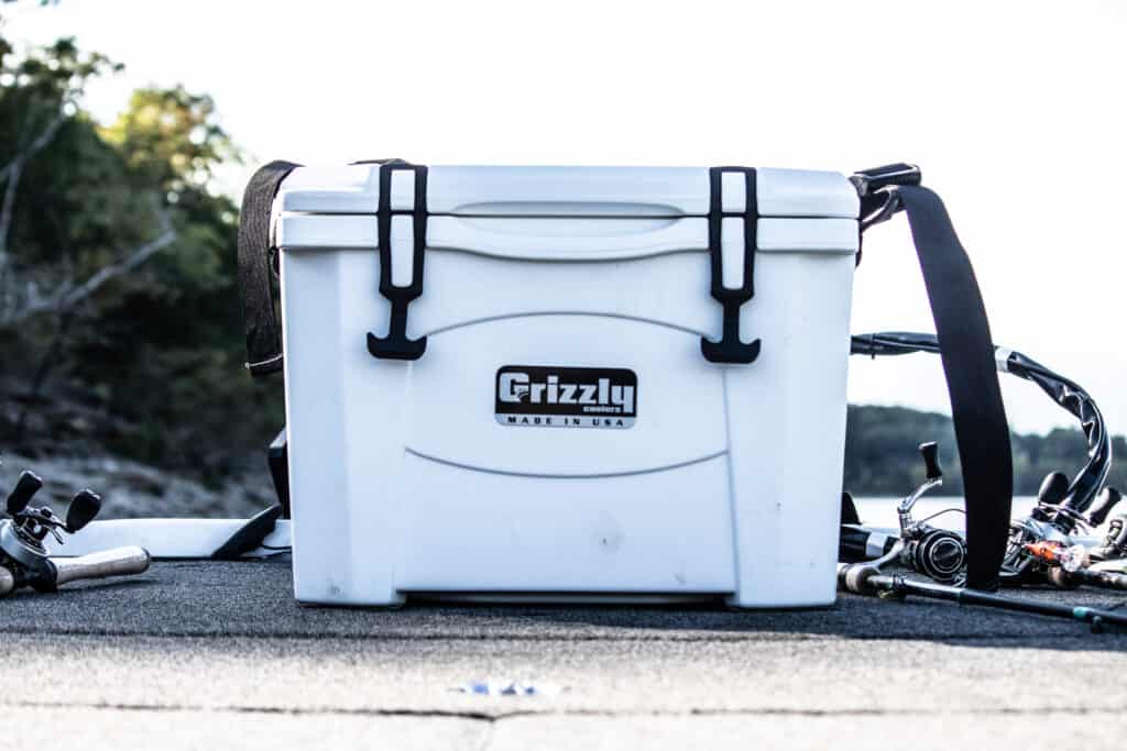 white grizzly 15 boat cooler sitting on bow of boat open with fishing rods and reels on either side and water and water front scenery in background