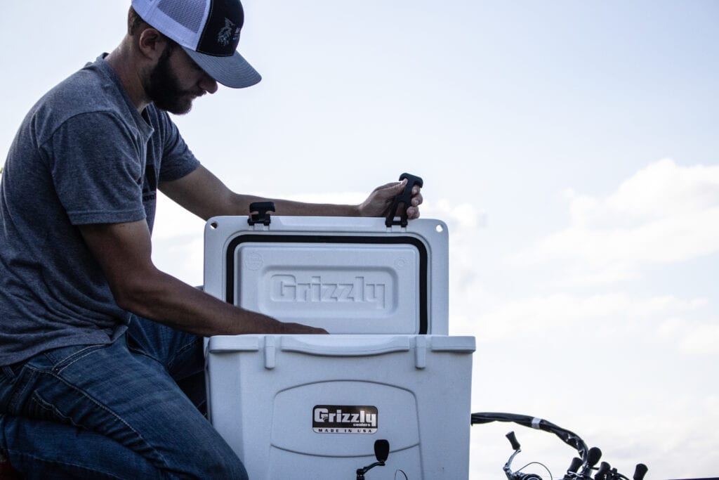 fisherman on bow of boat reaching into an opened grizzly 15 white boat cooler