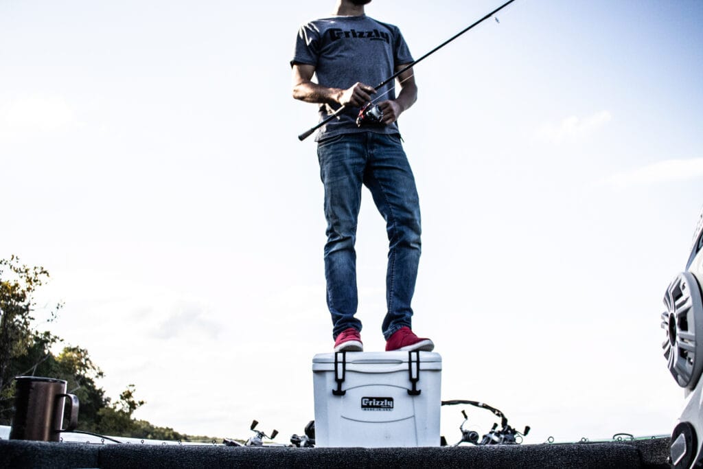 angler standing on white grizzly 15 boat cooler while reeling