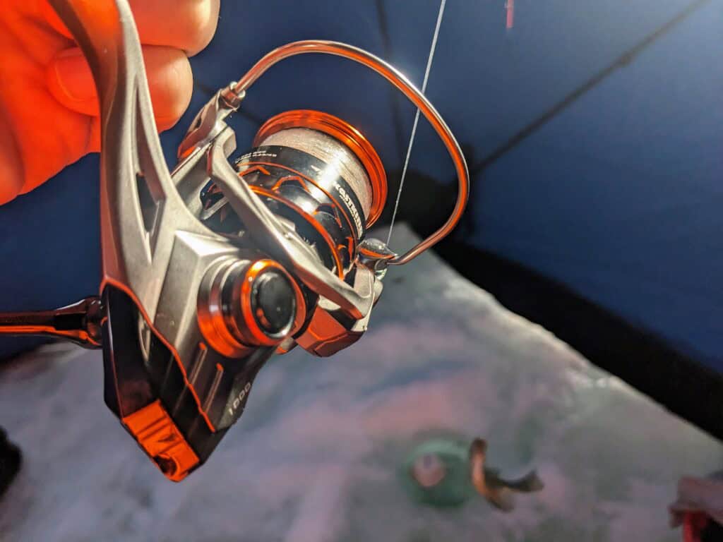 kastking kestrel spinning reel ice fishing in use very focused, with a fish caught, coming out of ice hole in the background and unfocused.