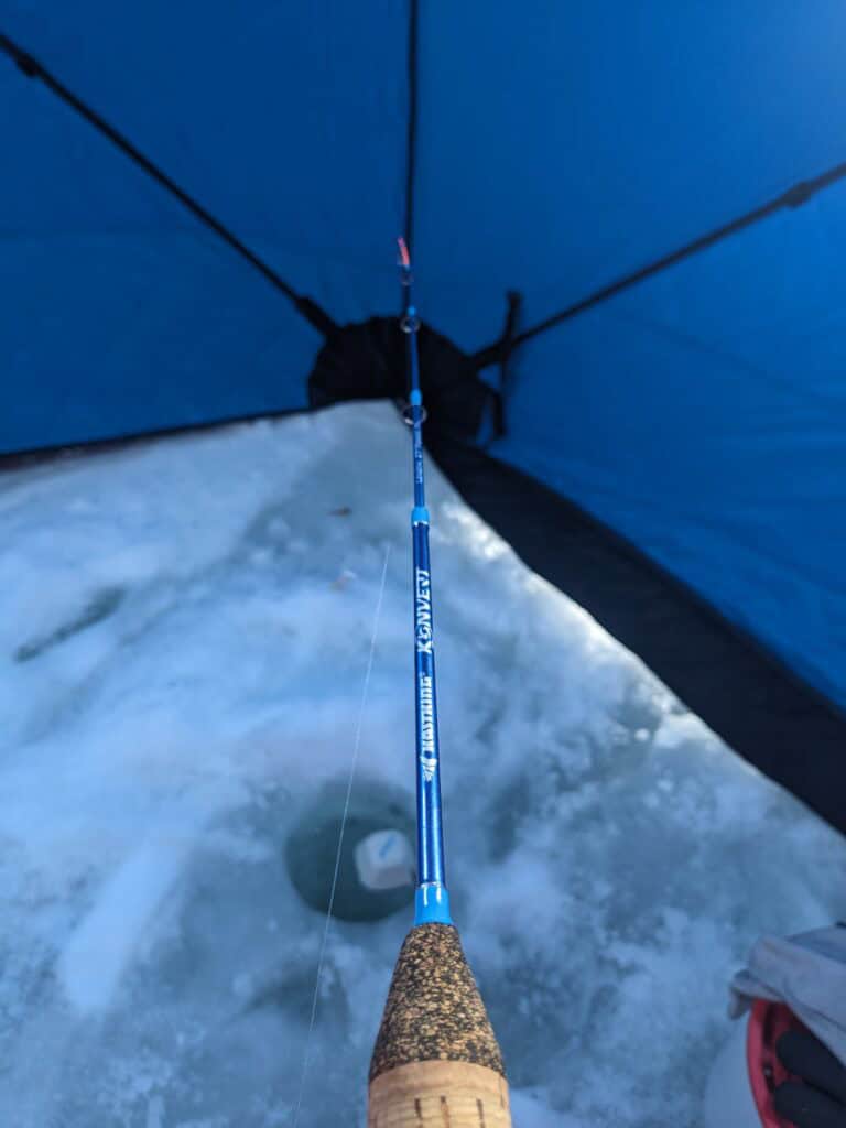 KastKing Konvert ice fishing rod in use over ice hole in ice fishing pop up shelter